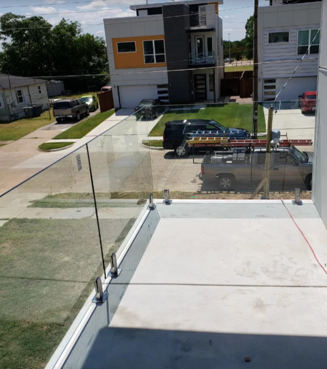 Glass balcony railing with city and hills in the background, in soft daylight