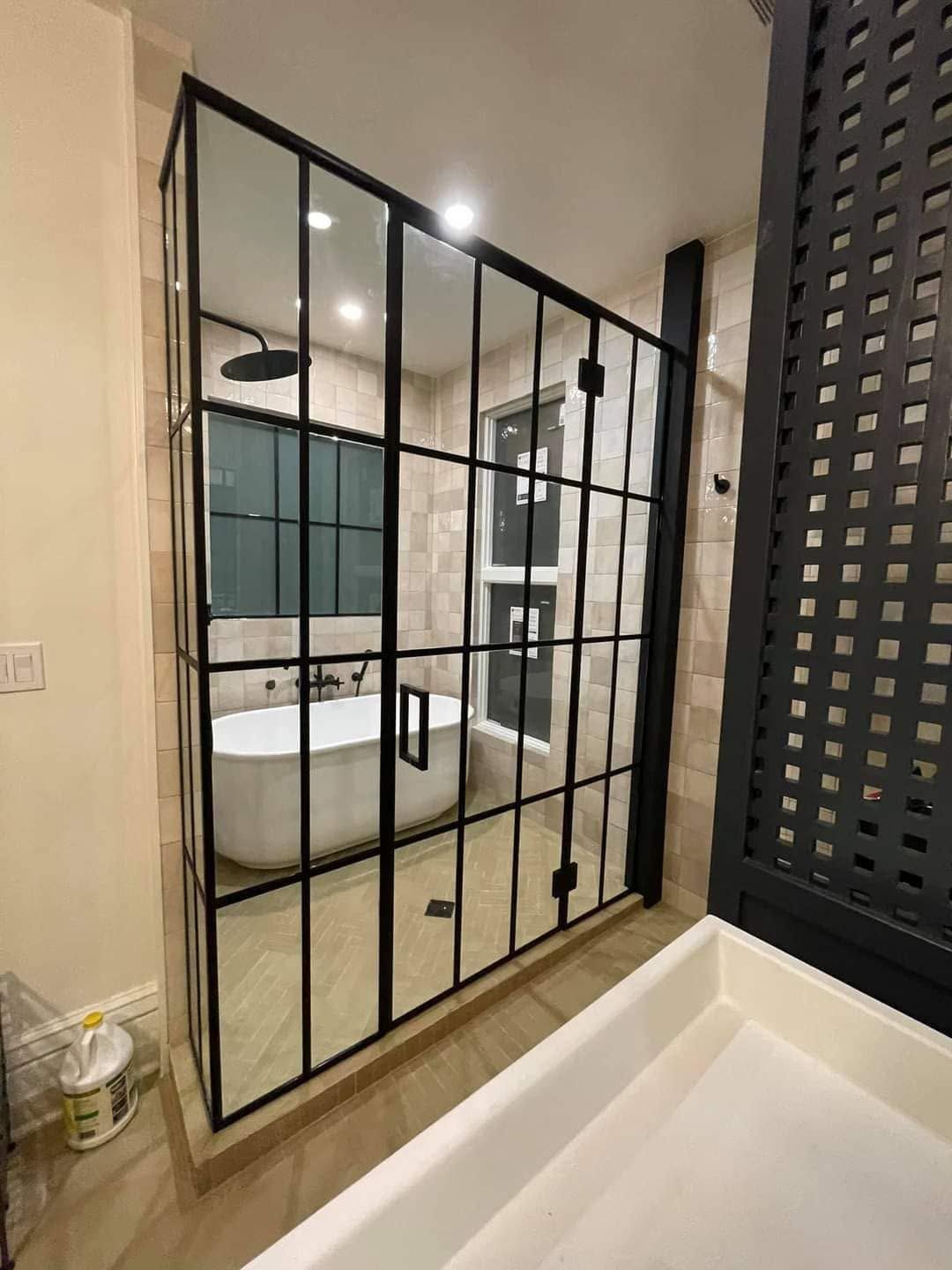 Modern bathroom with glass shower doors, white tub, and black tiled accent wall