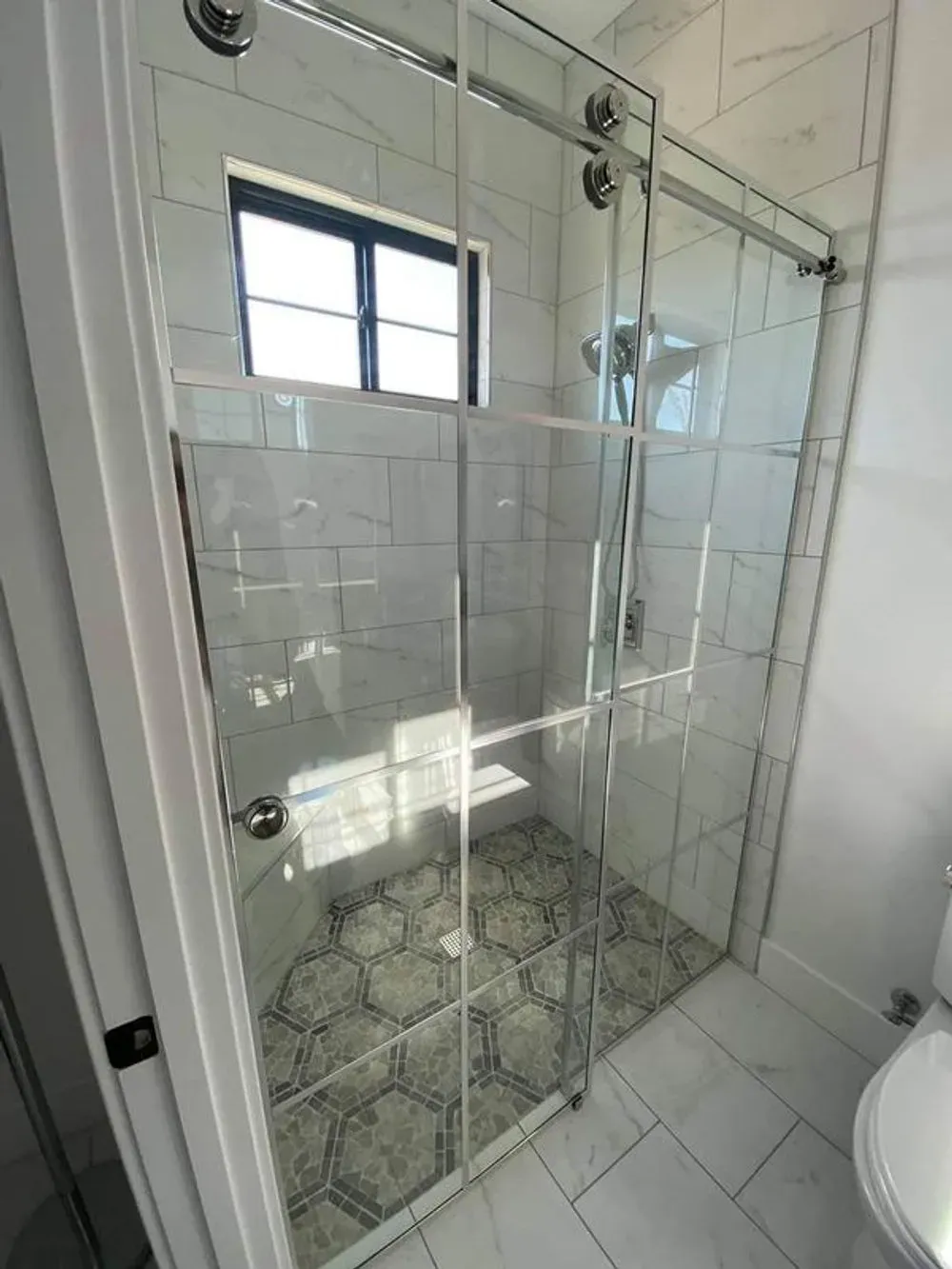 Glass shower enclosure with white tile walls and patterned floor in a bathroom