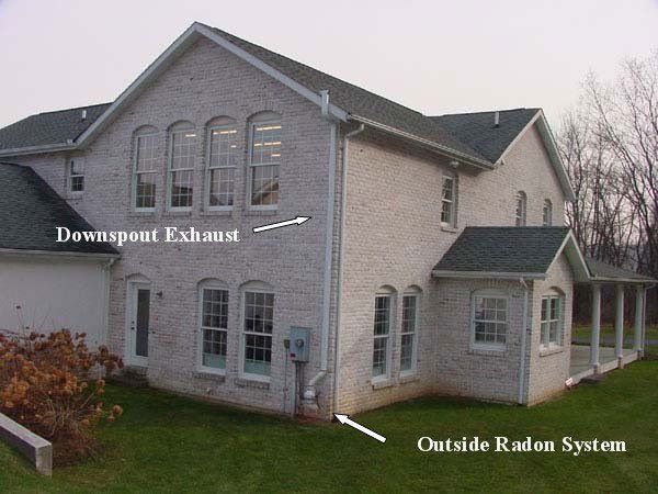 a brick house with a downspont exhaust and an outside radon system