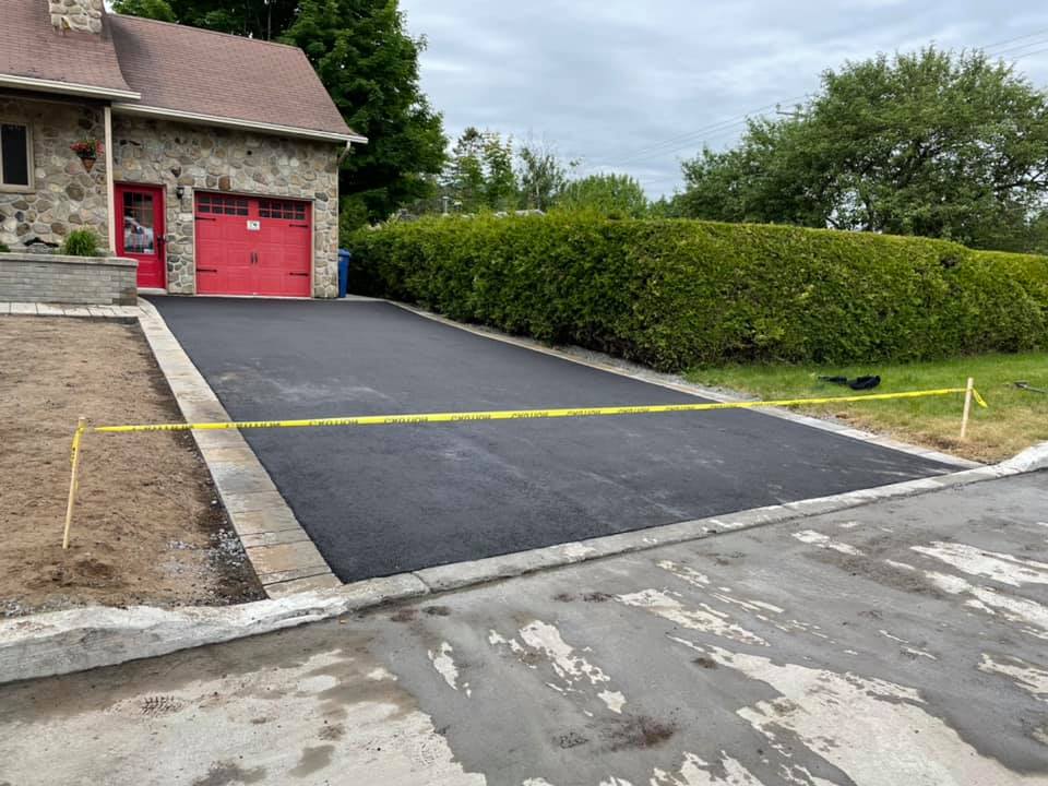 Une allée est en cours de construction devant une maison avec une porte de garage rouge.
