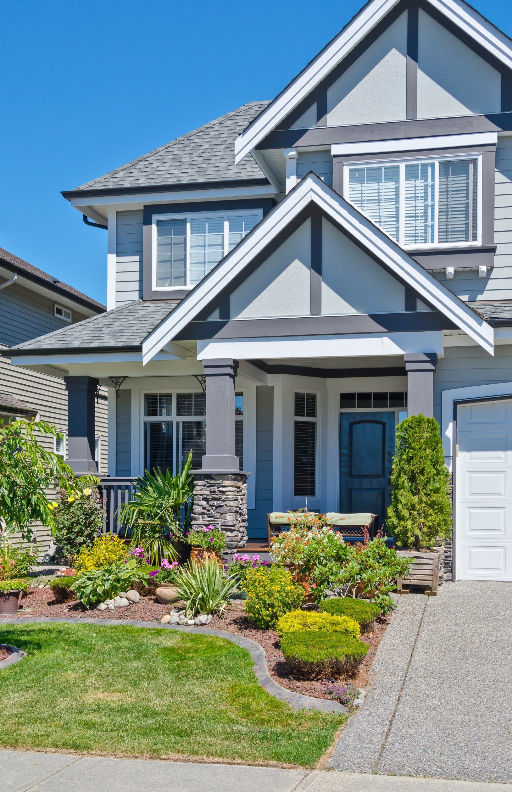 Une grande maison avec un toit gris et des garnitures blanches est assise sur une pelouse verte luxuriante.