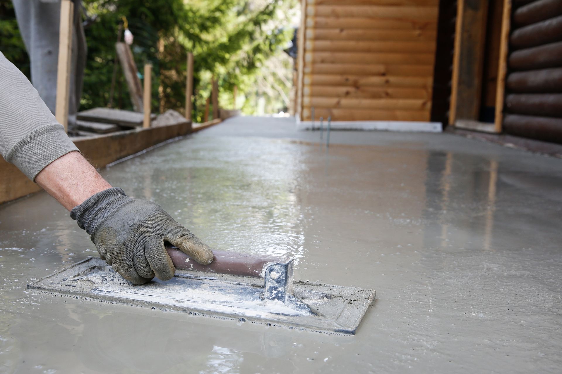 A mason using a level and screed to smooth and level a concrete floor base.