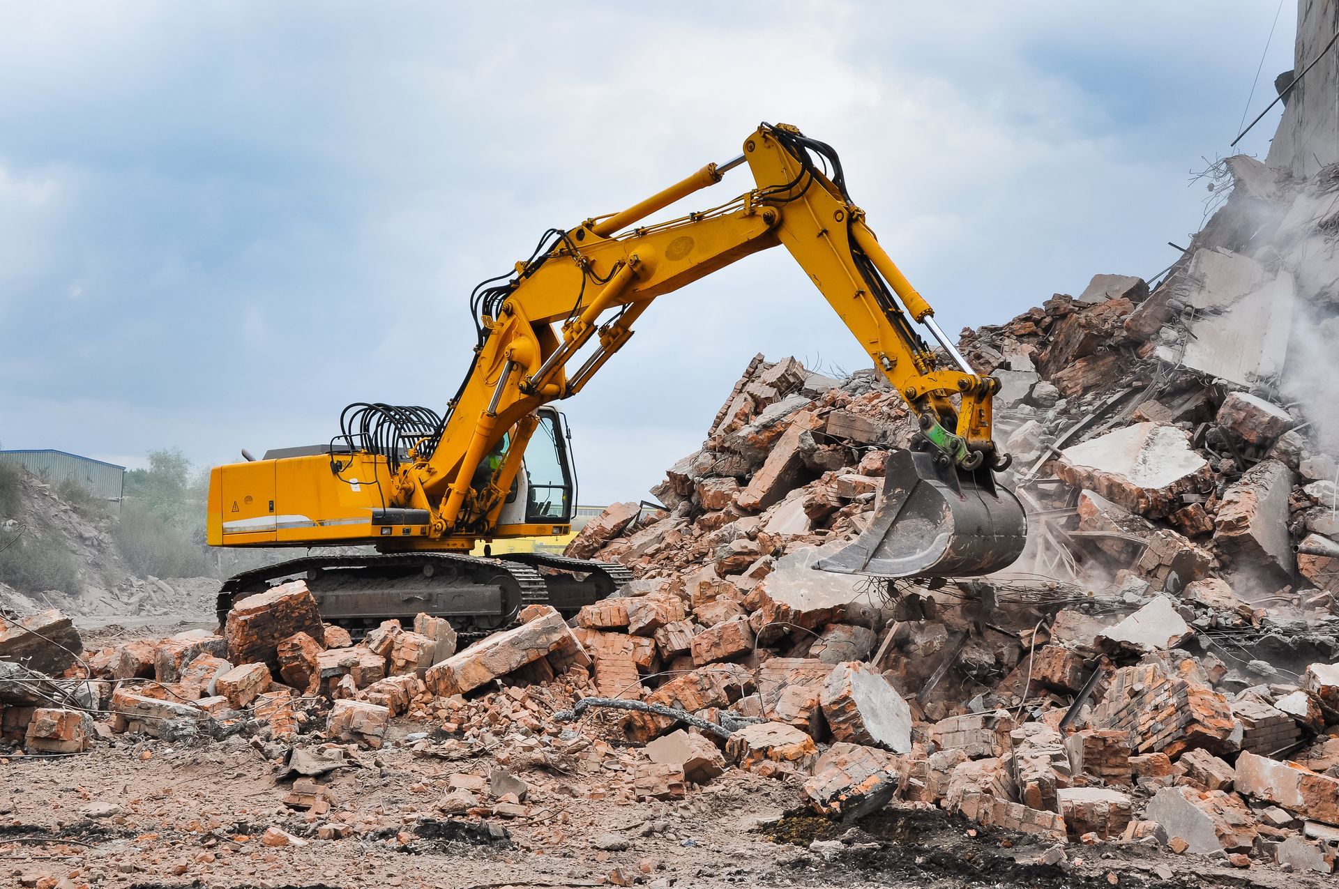 Excavator demolishing an old industrial building, with debris flying in the air.