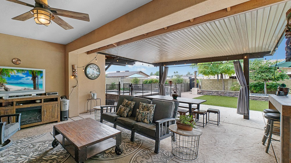 an outdoor living room with a couch , table , television and ceiling fan .