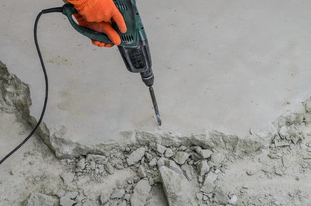 a person wearing orange gloves is using a drill to break concrete