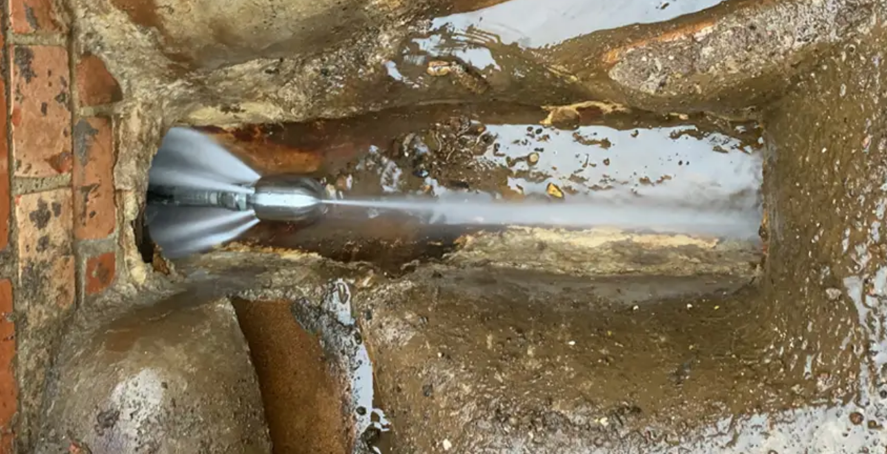 Jet nozzle spraying water inside a dirty pipe drain, removing debris.