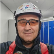 Man in veiligheidsuitrusting: witte helm, oranje bril, blauwe kluisjes op de achtergrond.