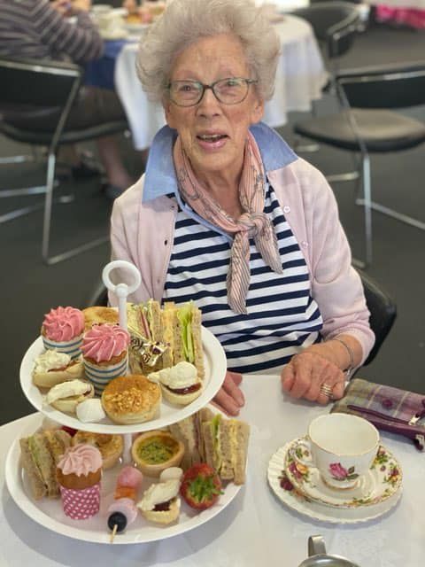 An elderly woman is sitting at a table holding a plate of food.