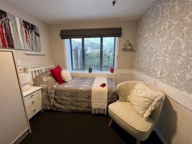 A bedroom with a bed , chair , nightstand and window.