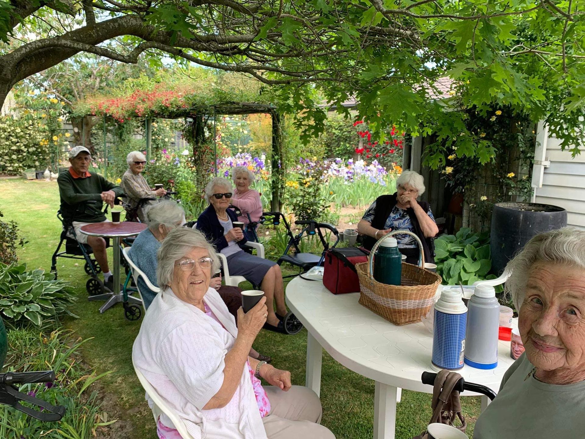 A group of elderly people are sitting around a table in a garden.