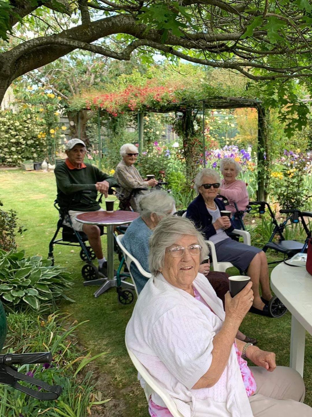A group of elderly people are sitting at tables in a garden.
