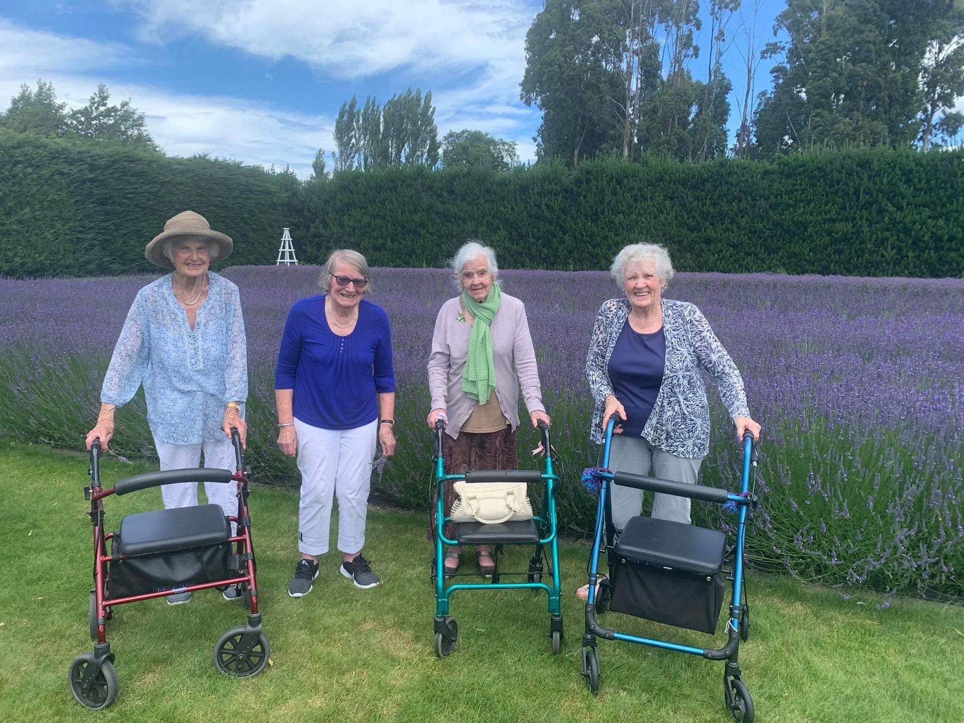 A group of elderly women standing in front of a lavender field with walkers.