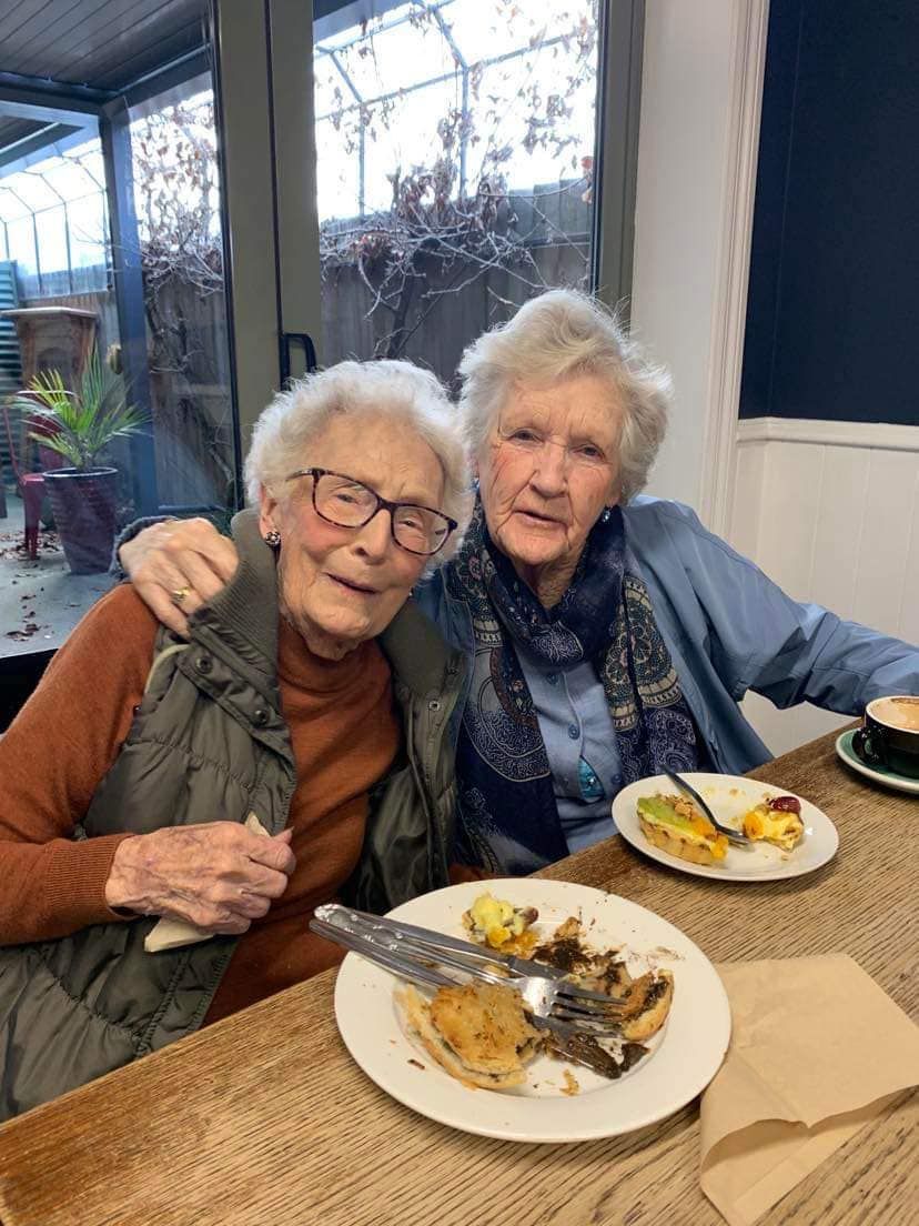 Two older women are sitting at a table with plates of food.