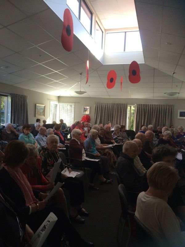 A large group of people are sitting in a room with red poppies hanging from the ceiling.