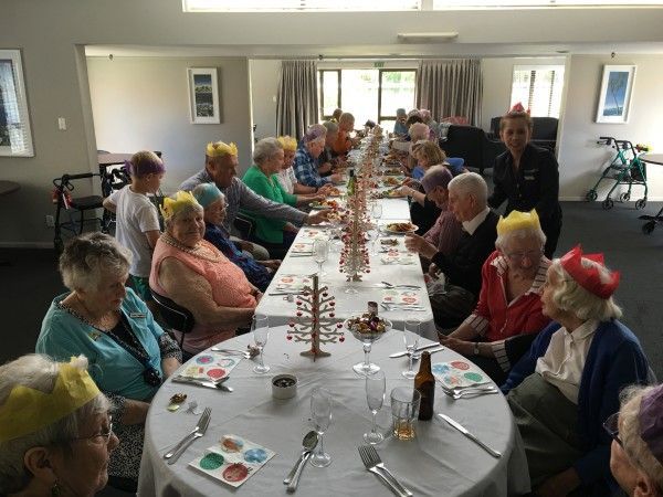 A group of elderly people are sitting at a long table wearing crowns.