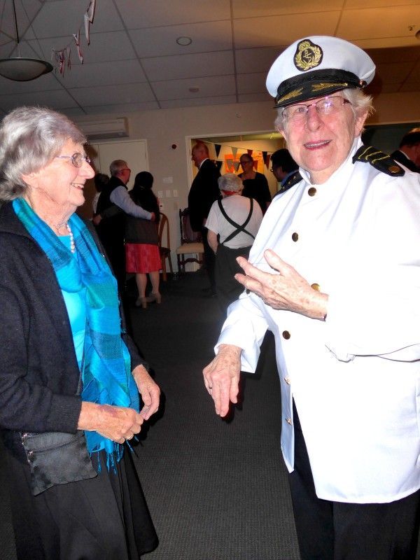 A man in a captain 's hat talks to a woman in a blue scarf