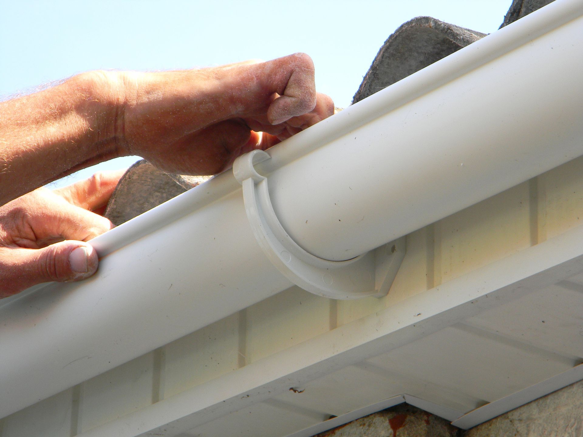 A person is installing a white gutter on a roof.