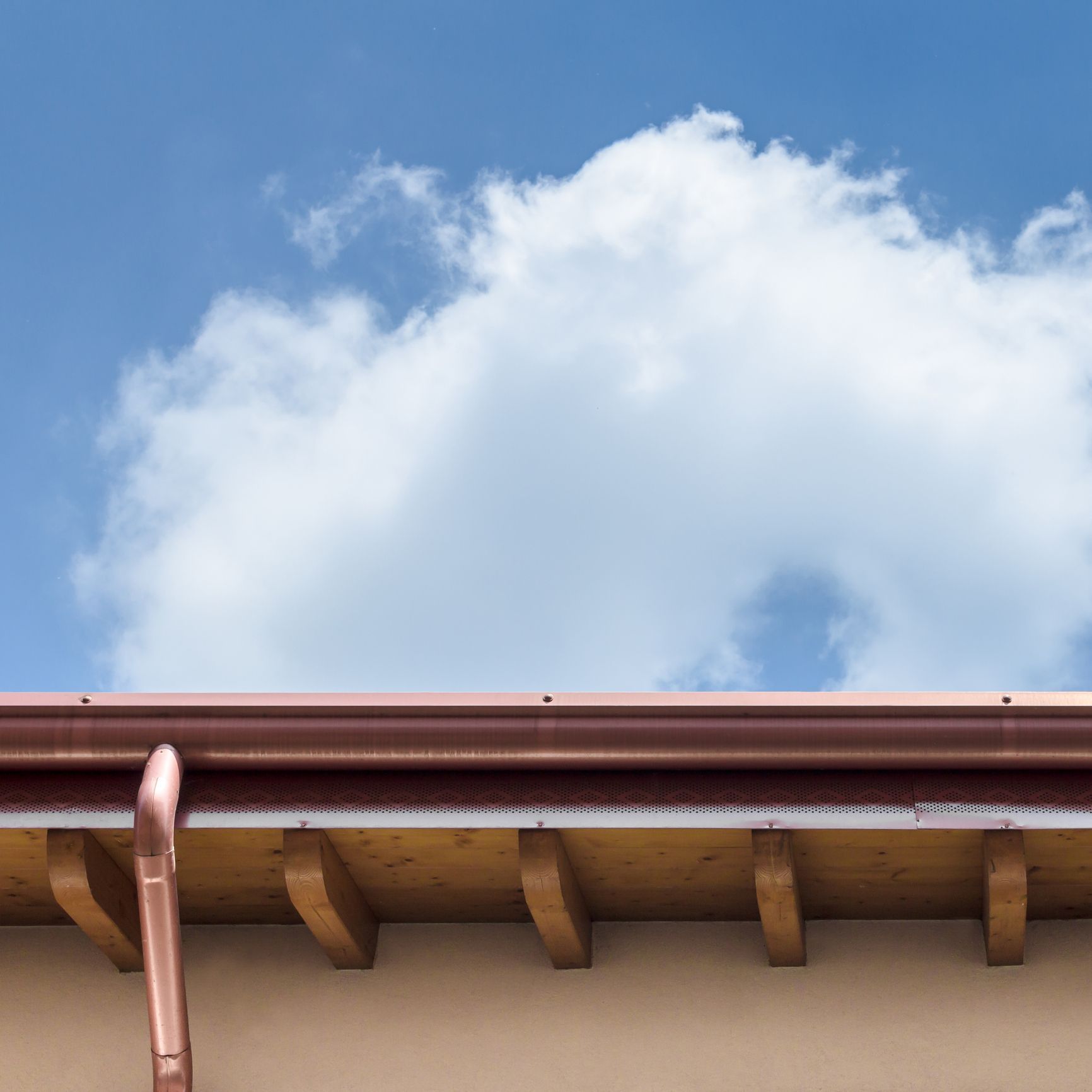 A copper gutter on the roof of a building with a blue sky in the background.