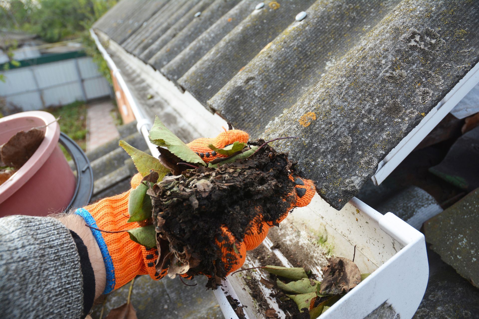 A person wearing orange gloves is cleaning a gutter on a roof.