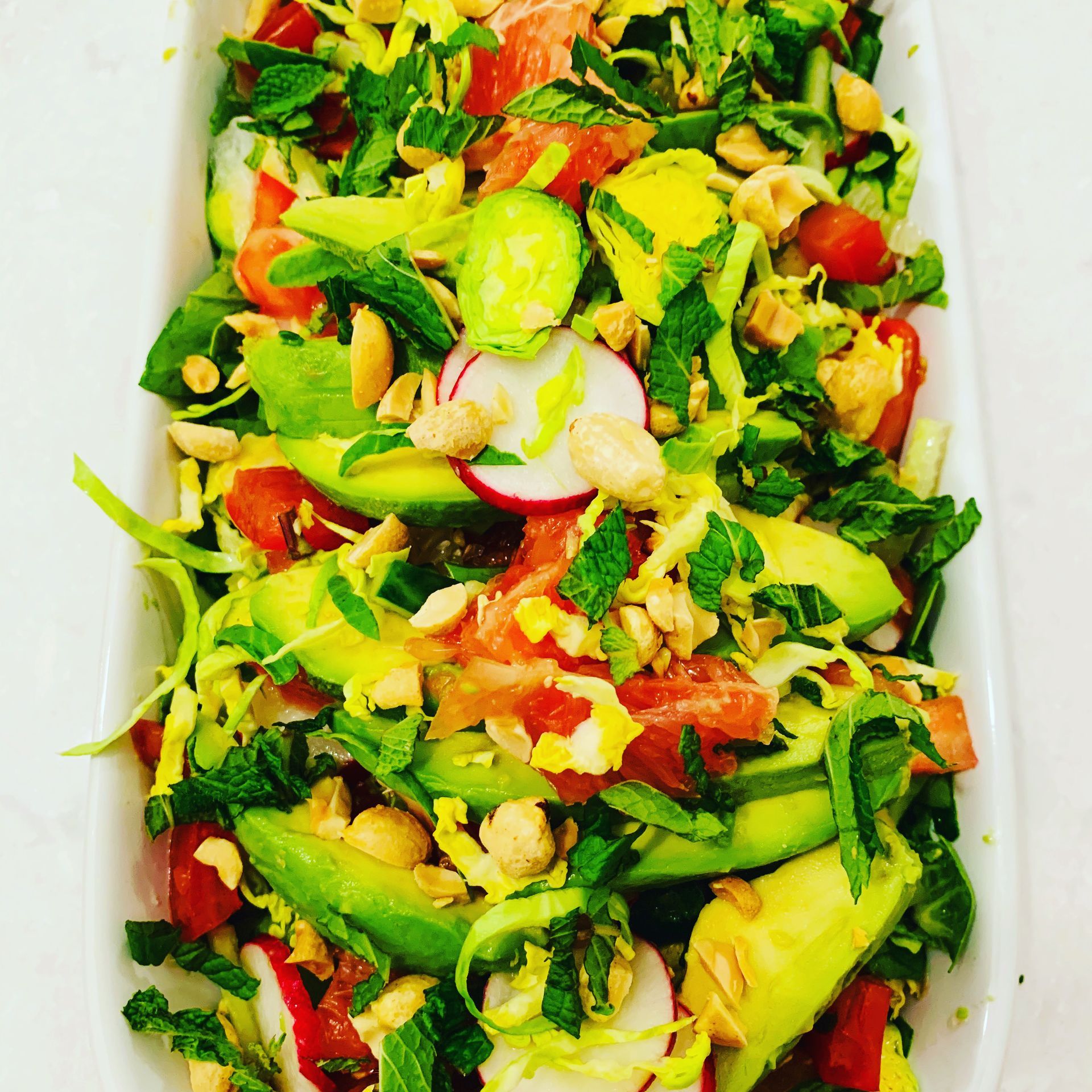 Salad with avocado, grapefruit, tomatoes, radishes, peanuts, and mint in a white dish.