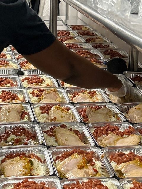 Person packing cooked chicken, beans, and rice into aluminum meal containers.