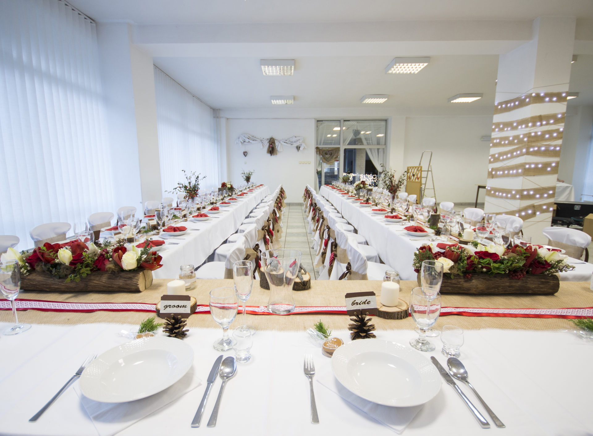 Long tables set for a wedding reception, white tablecloths, floral centerpieces, decorated venue.