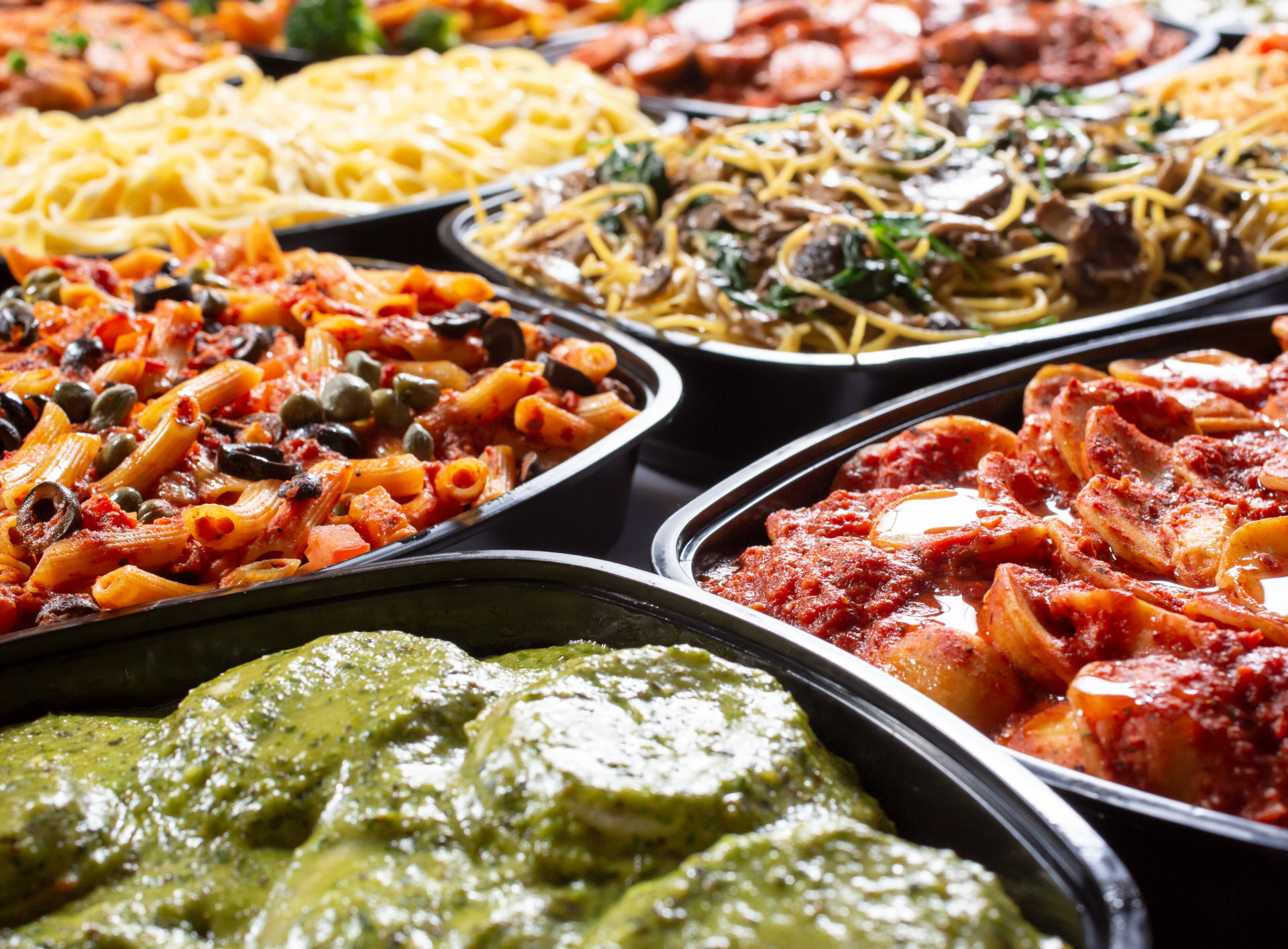 Pasta dishes in various sauces, served in black trays.