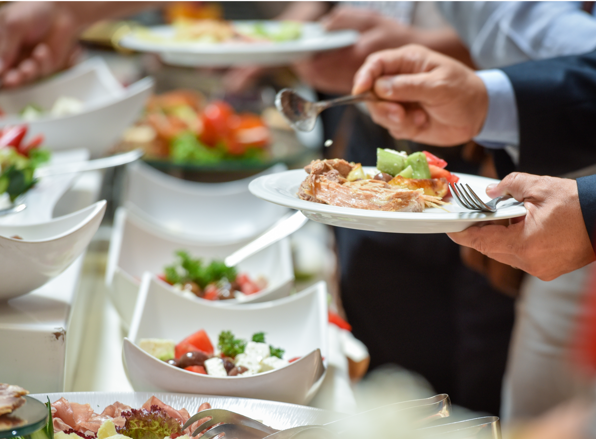 People serving food at a buffet, using serving utensils and plates.