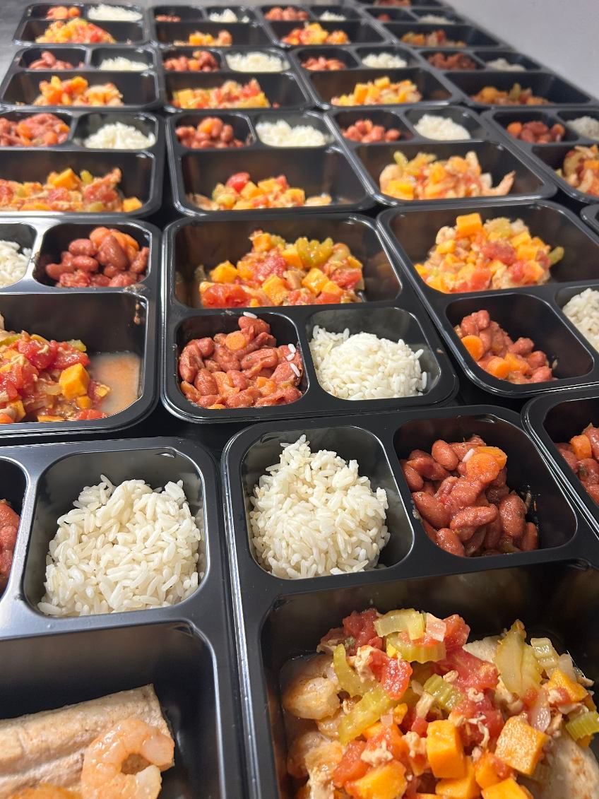 Rows of pre-portioned meal containers filled with rice, beans, and diced vegetables.