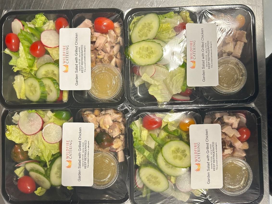 Four pre-packaged salads with lettuce, tomatoes, cucumbers, and chicken, with dressing containers.