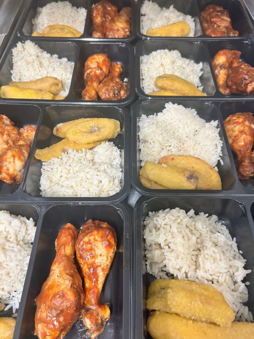 Prepared meal trays with rice, fried plantains, and chicken.