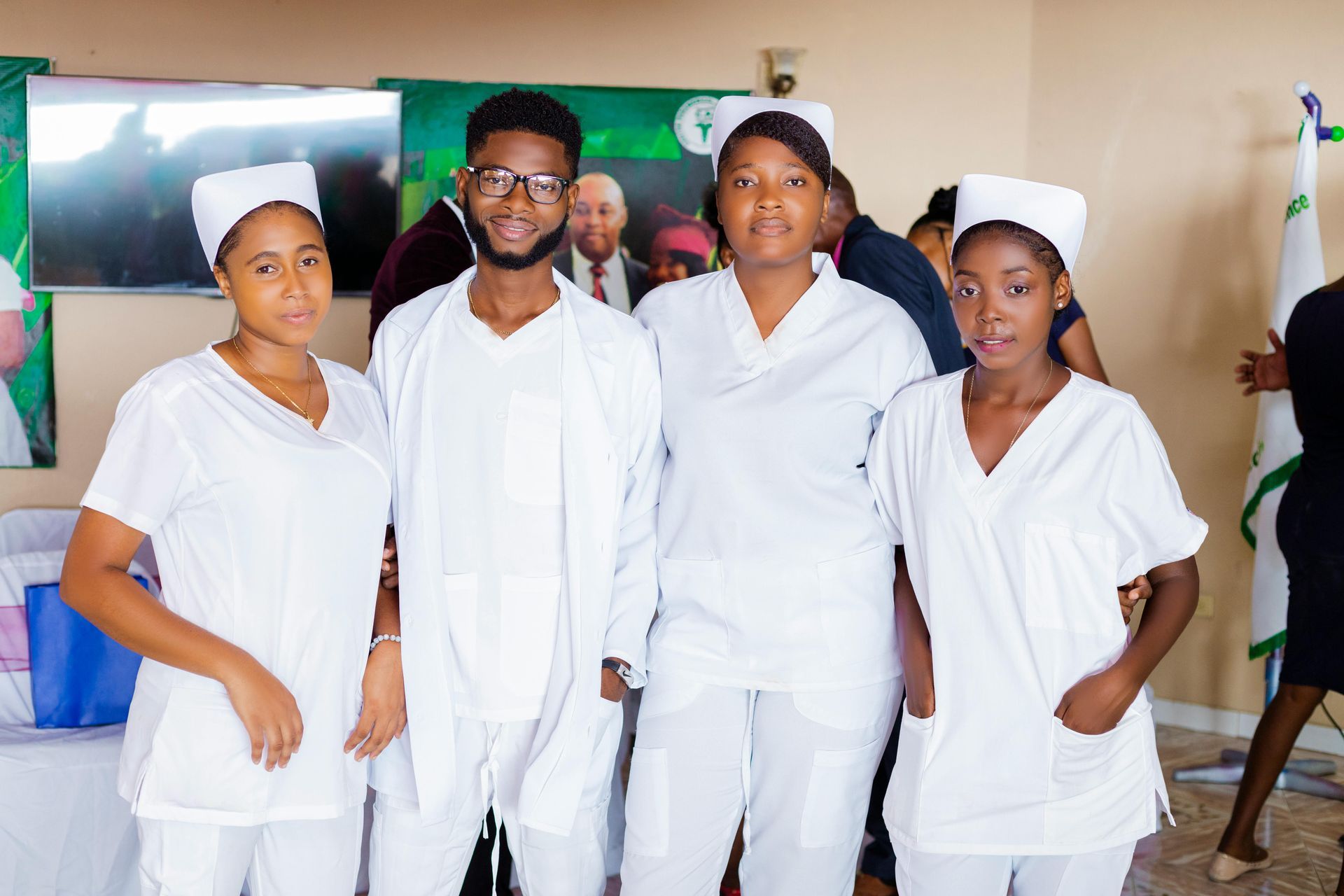 Four people in white uniforms pose in a room, two with caps.