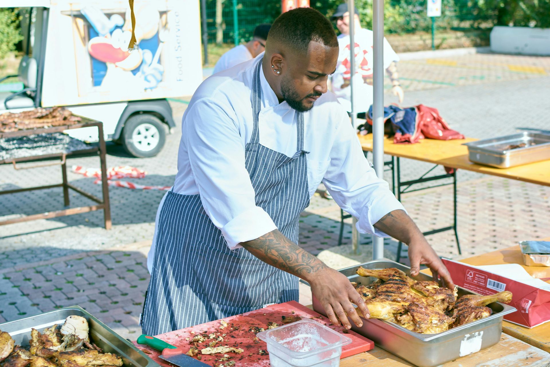Chef in white uniform and apron preparing food at an outdoor food stand.