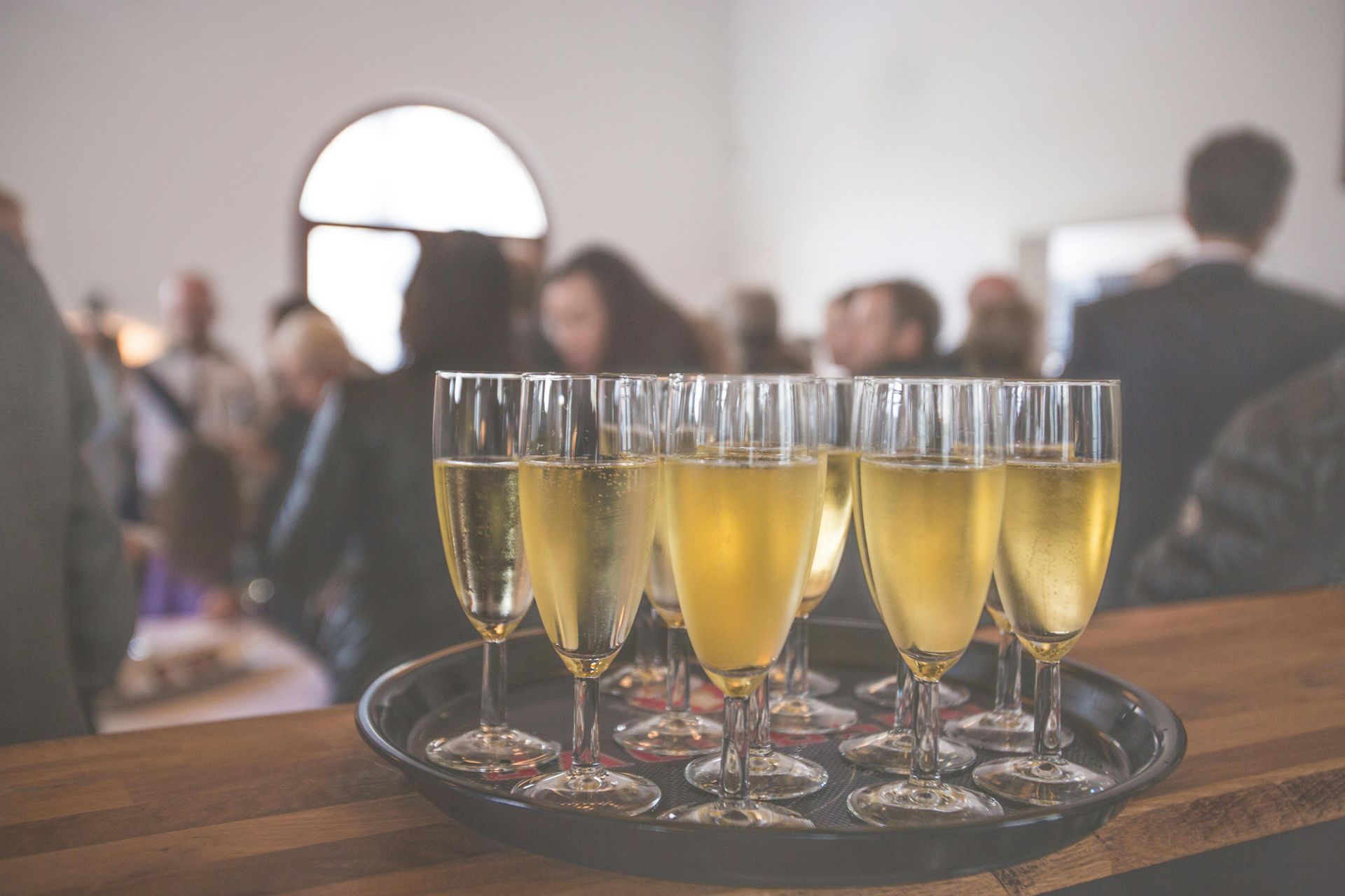 Tray of champagne flutes on a bar, with blurred figures in the background at an event.
