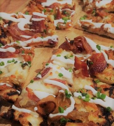 Flatbread with bacon, cheese, sour cream drizzle, and chives, on a wooden board.