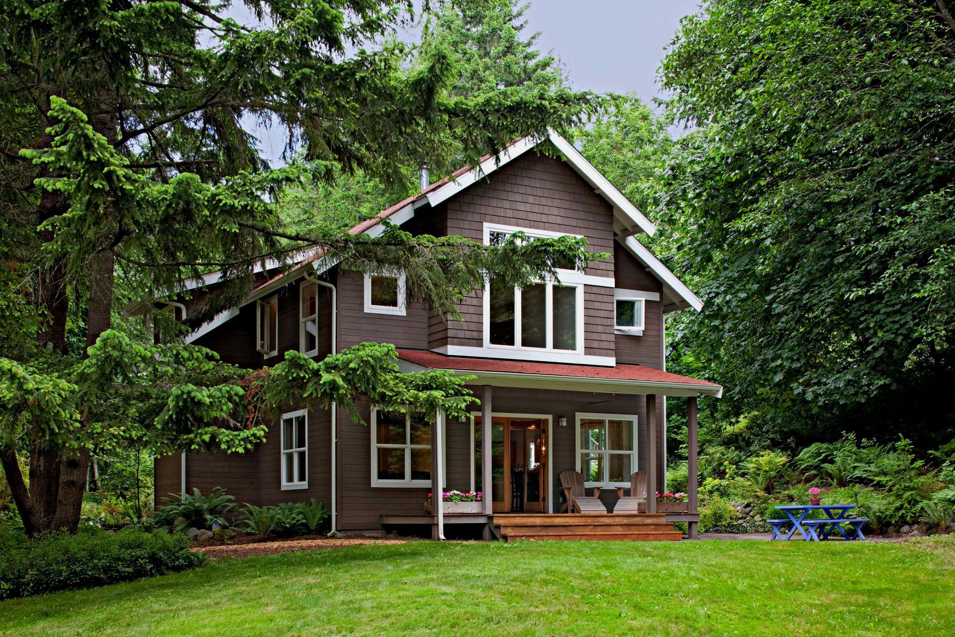 A brown house with a red roof is surrounded by trees