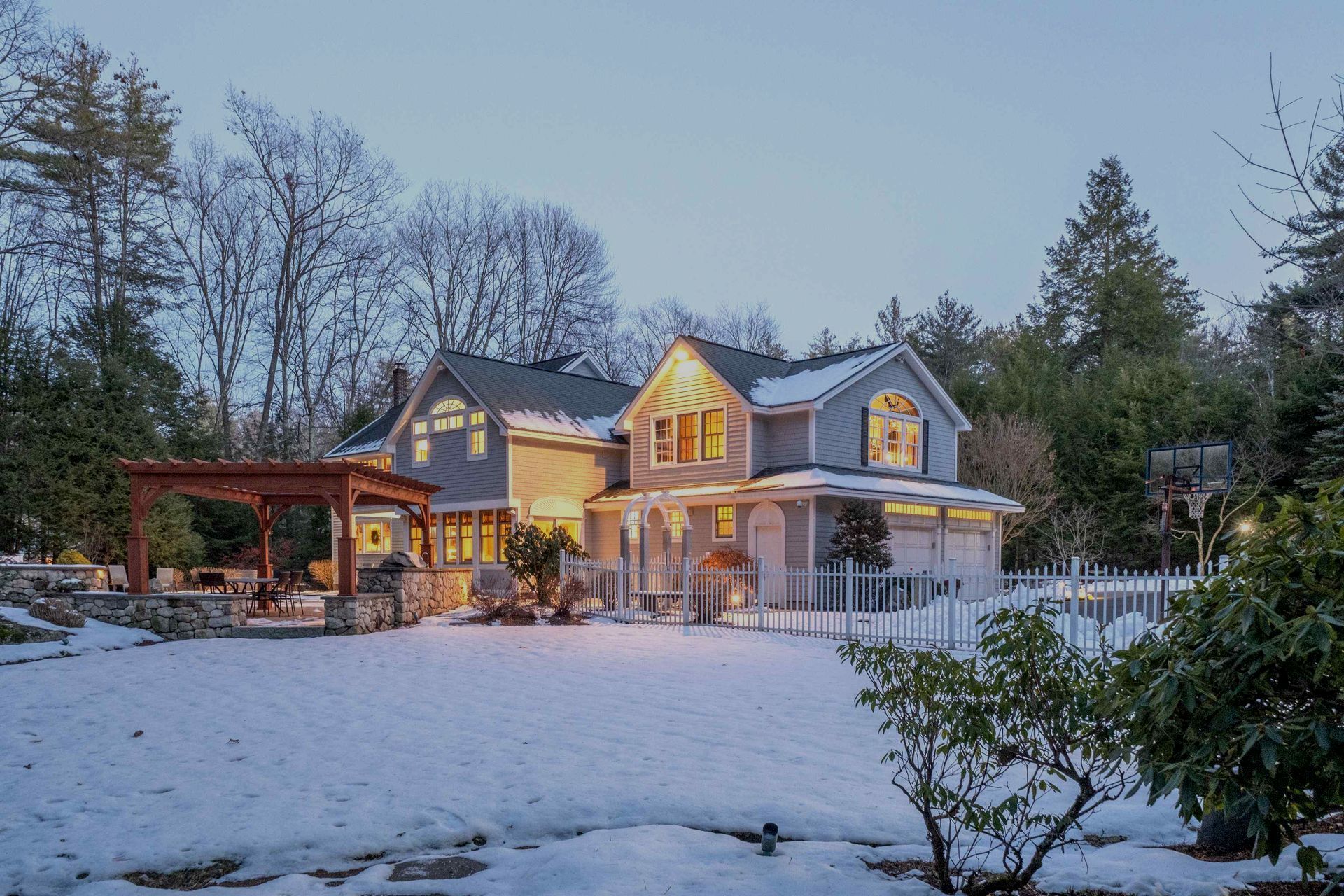 A large house is surrounded by snow and trees and is lit up at night.