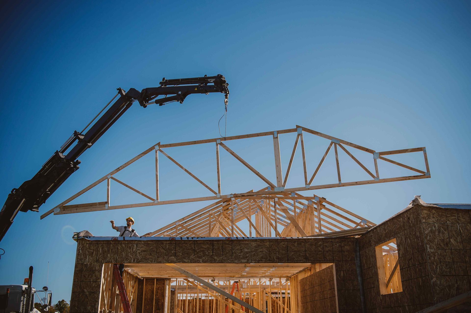A crane is lifting a wooden structure on top of a house under construction.