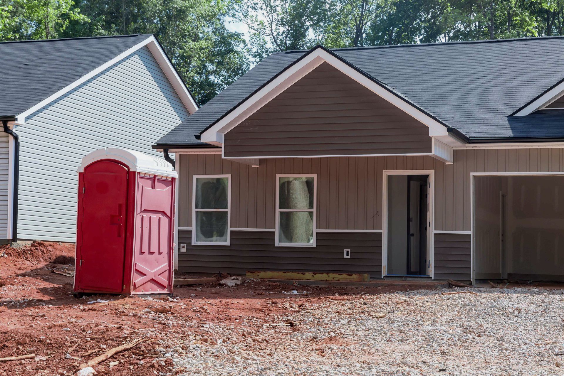 A house under construction with a red portable toilet in front of it.