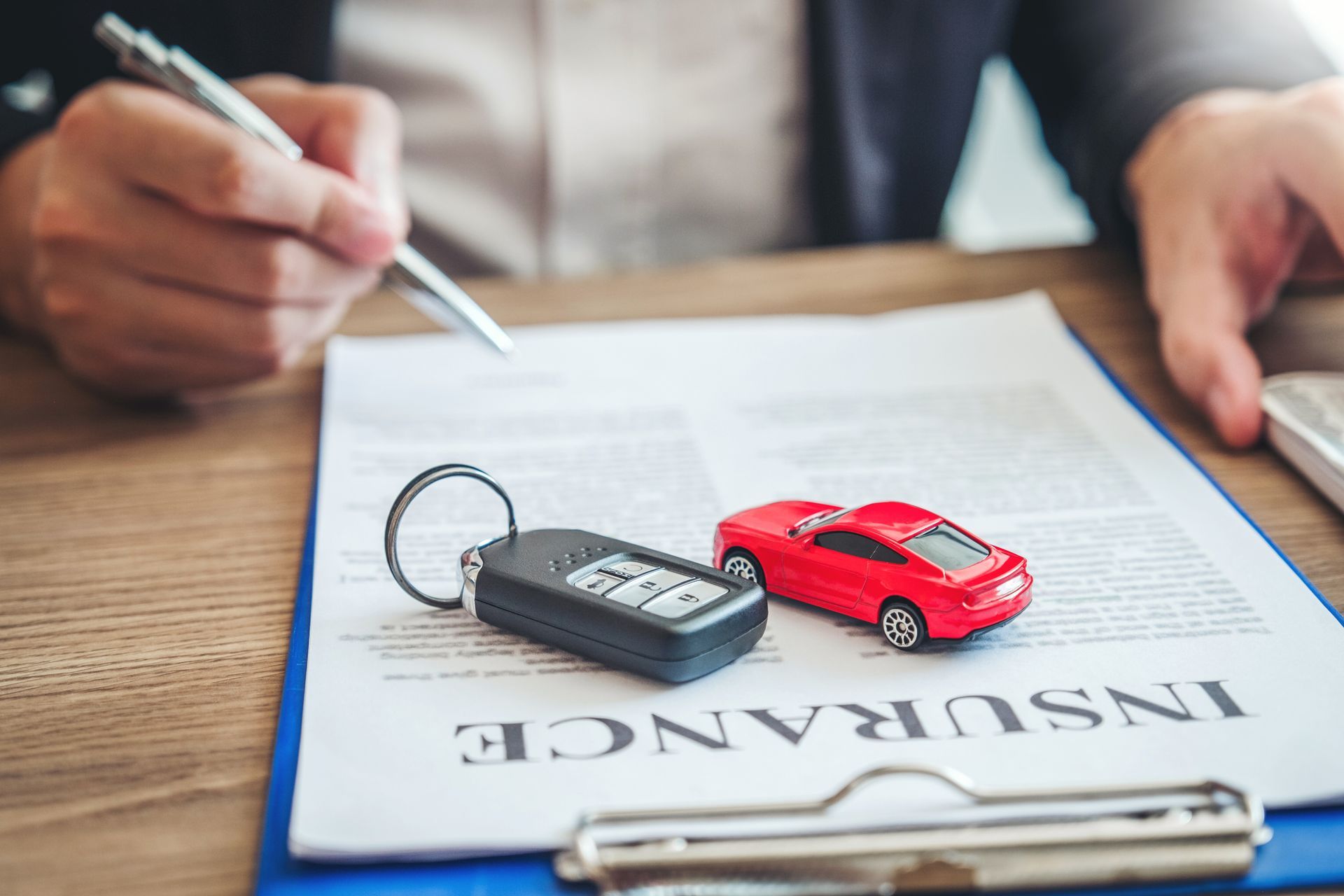 A customer signs a contract with a local auto insurance agency, keys, and a red car on paper.