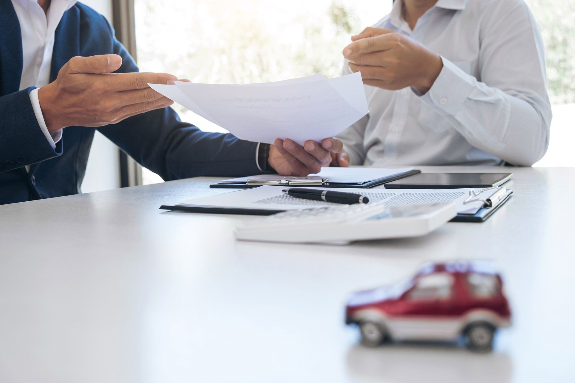 Insurance agent presents a document to a client, with a blurry toy car close to the camera - Loganville, GA - Taurus Insurance
