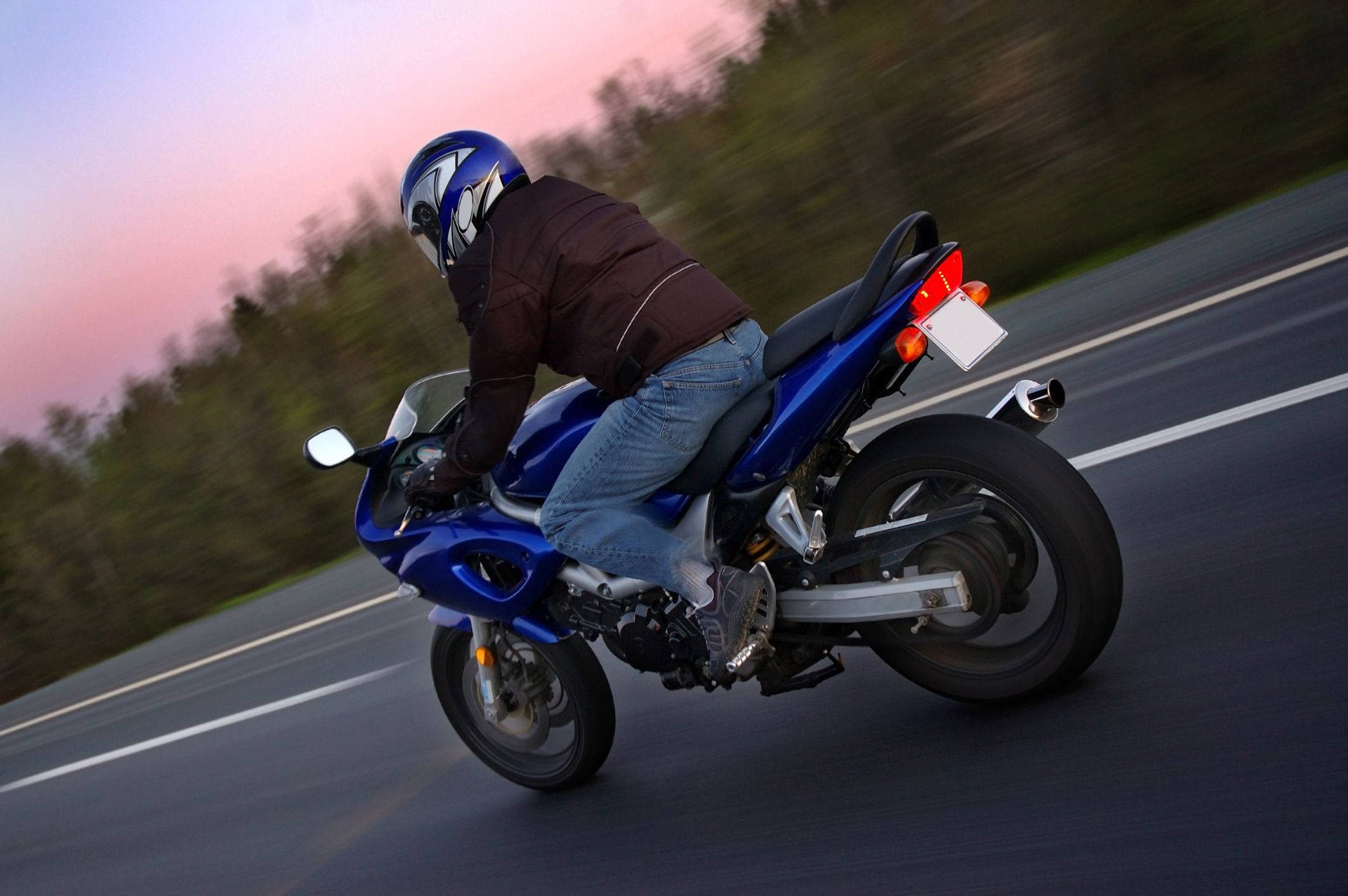 A rider is on a sport motorcycle riding at full speed in the twilight.