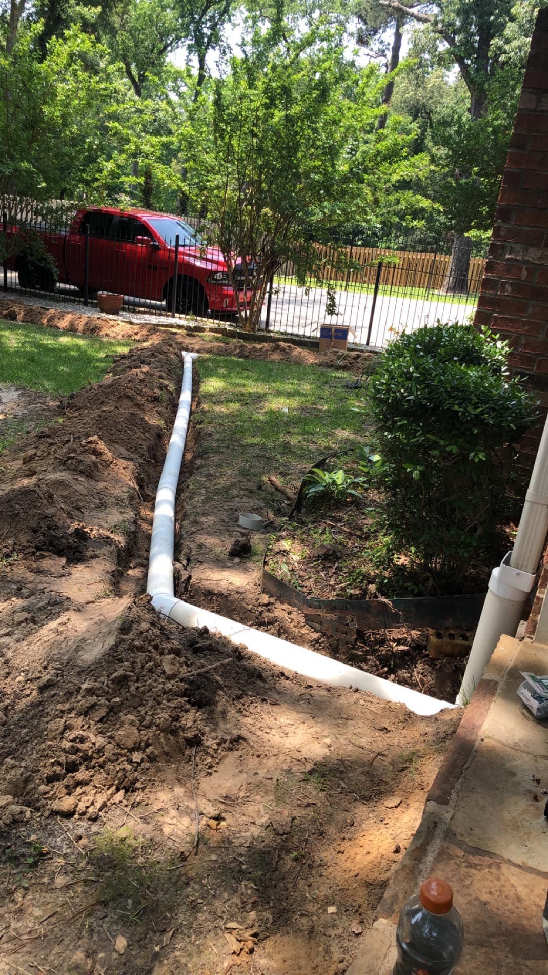 A red truck is parked in the driveway of a house next to a drain pipe.