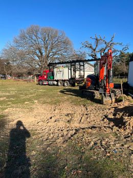 A red truck is driving down a dirt road next to a small excavator.