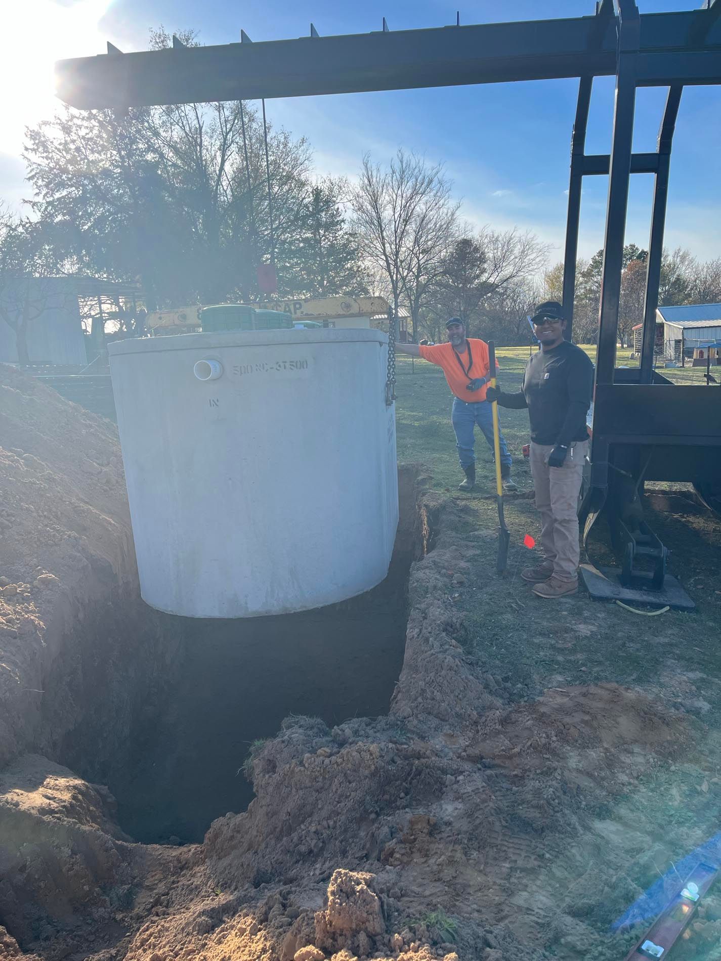 Two men are digging a hole in the ground next to a large concrete cylinder.