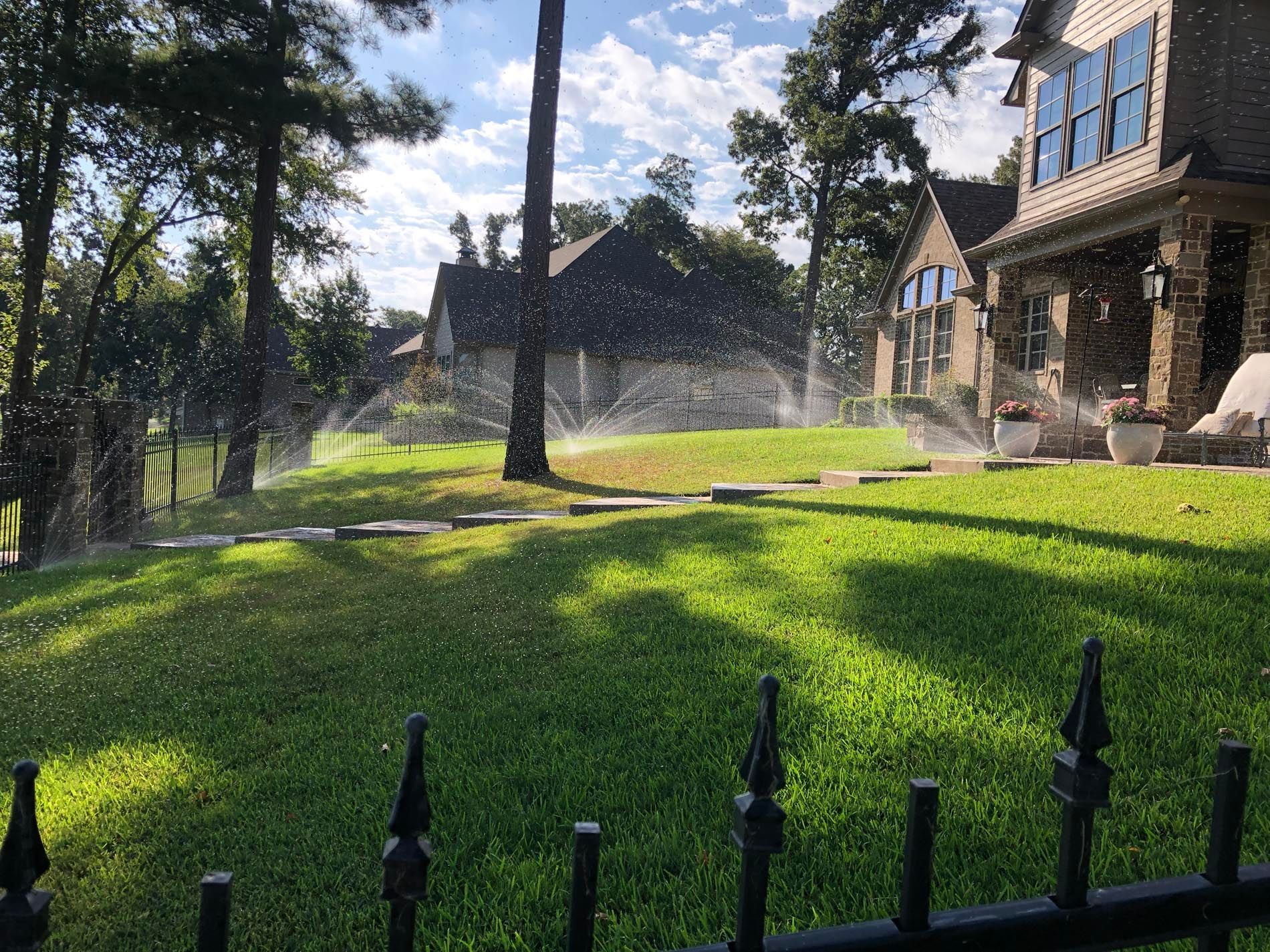 A sprinkler is spraying water on a lush green lawn in front of a house.