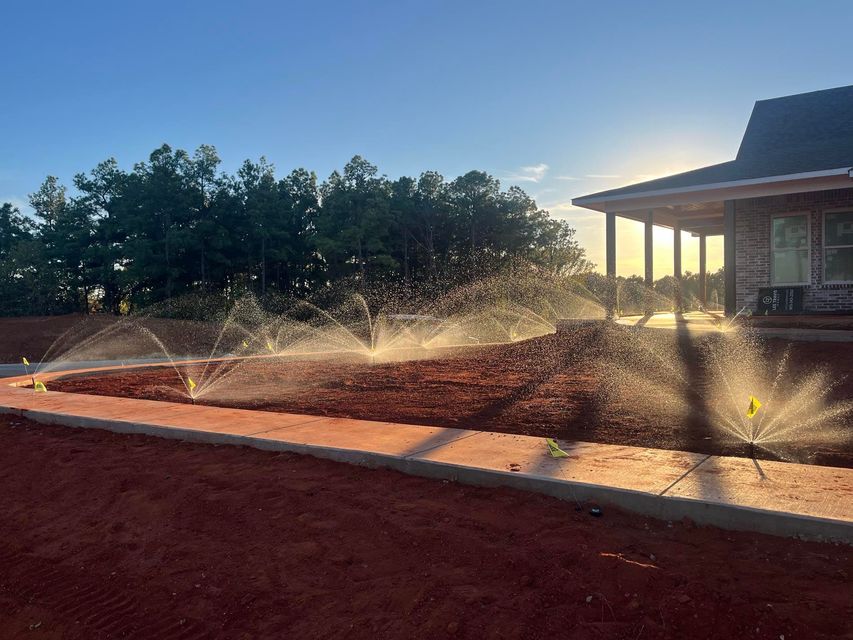 A sprinkler is spraying water on a dirt field in front of a house.