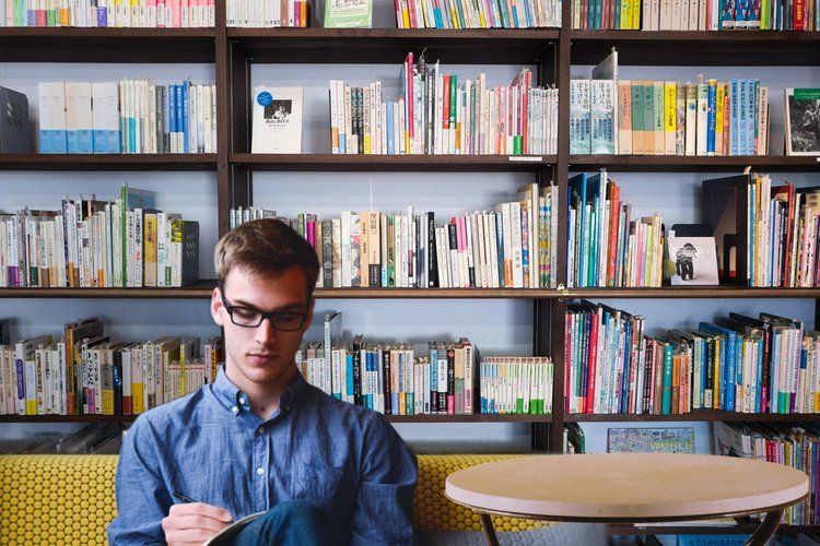 A man is sitting at a table reading a book in a library.