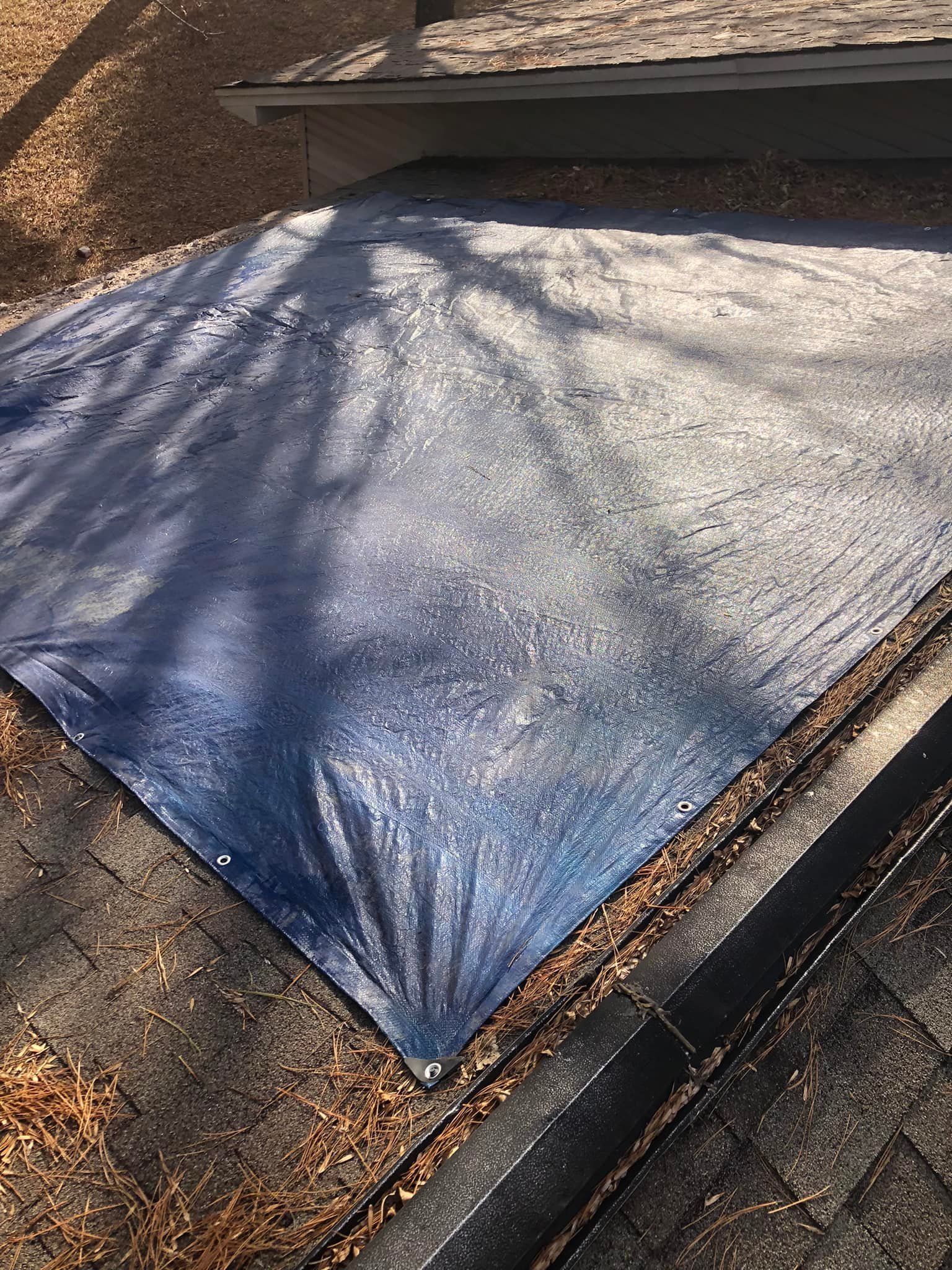 Blue tarp covering a section of a weathered roof with visible water droplets.